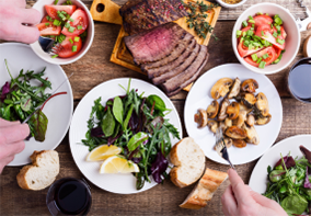 Vollgestellter Tisch mit Tellern mit Salat, Kartoffel und Fleisch